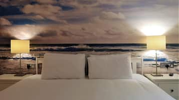 Una cama con sábanas blancas, dos lámparas de noche y vistas al océano a través de una ventana.