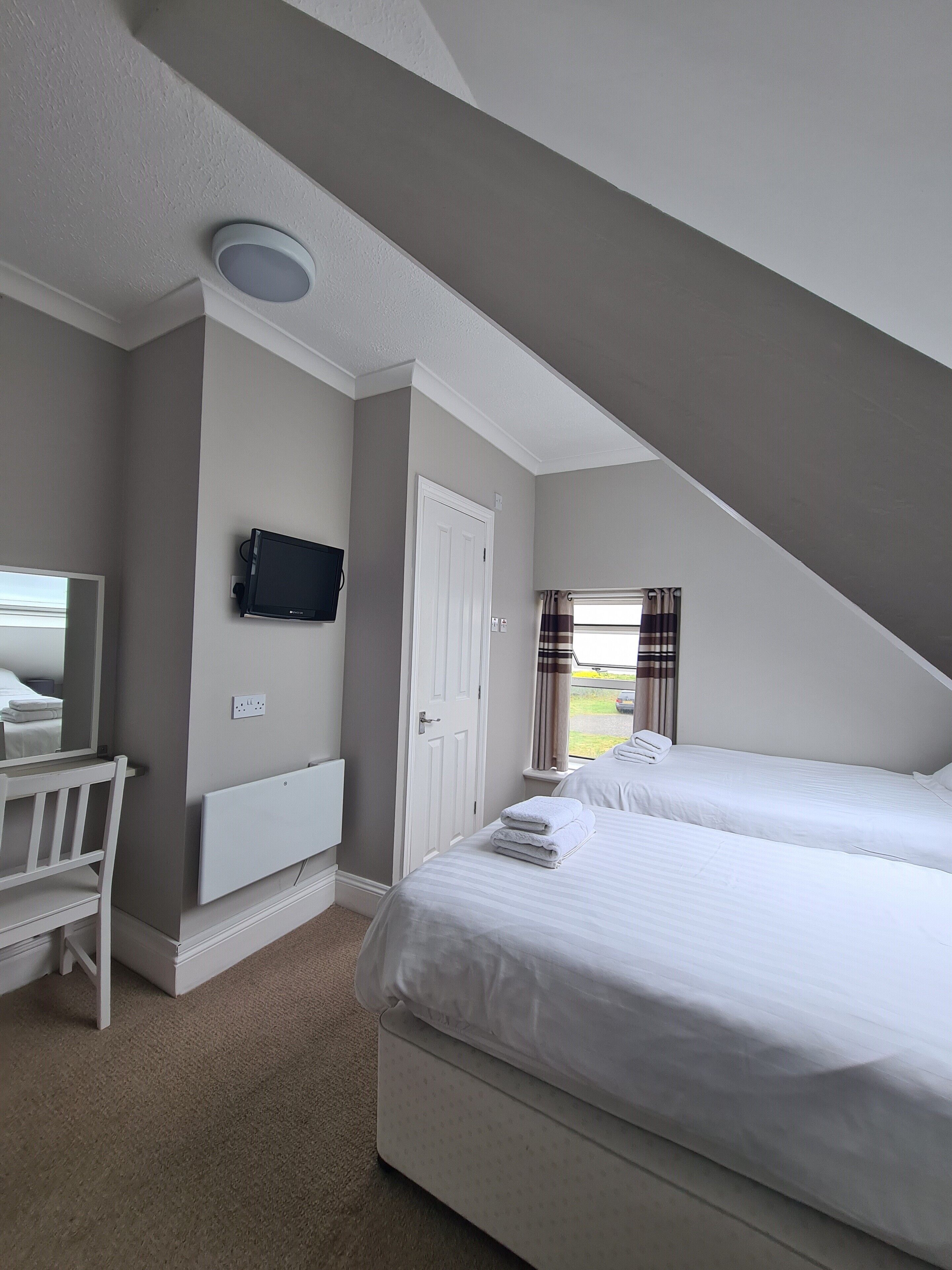 A bedroom with two beds, a television, a mirror, and a window with curtains.