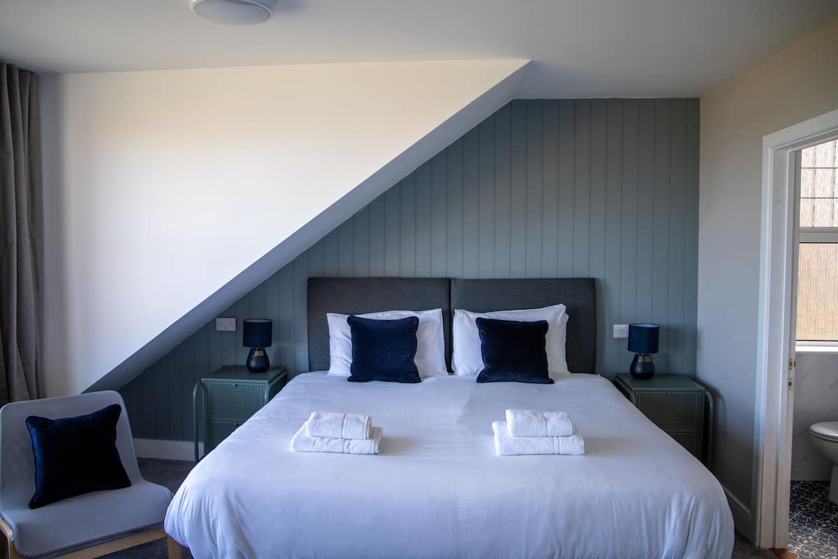 A hotel room with a large bed, two nightstands, a chair, and a view of the outside.