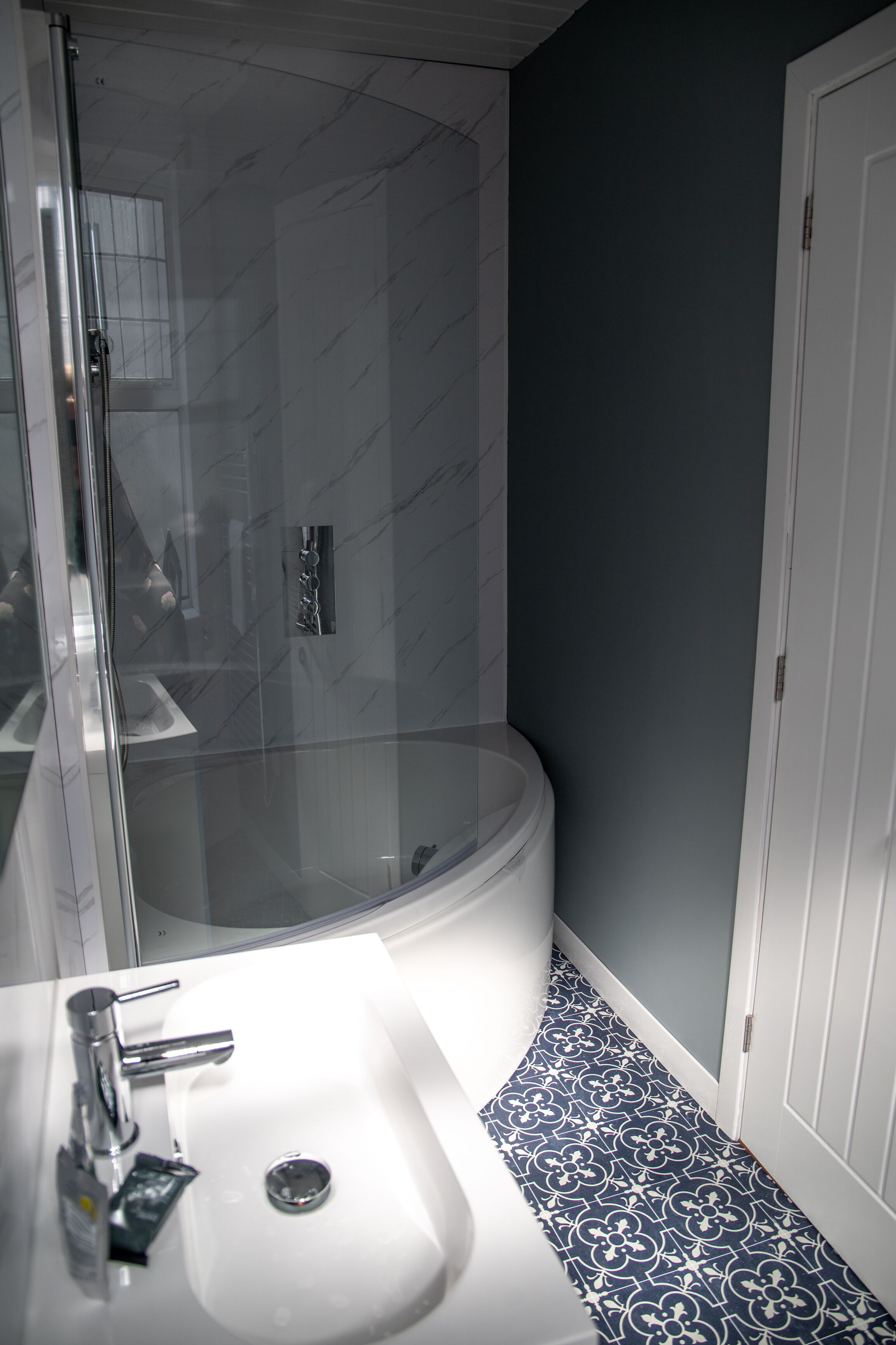 A modern bathroom with a glass-enclosed shower, a white sink with chrome fixtures, and patterned floor tiles.