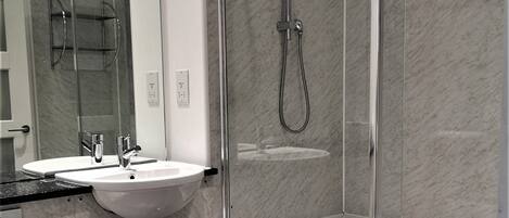 A modern bathroom with a glass-enclosed shower, a white sink, and a toilet.