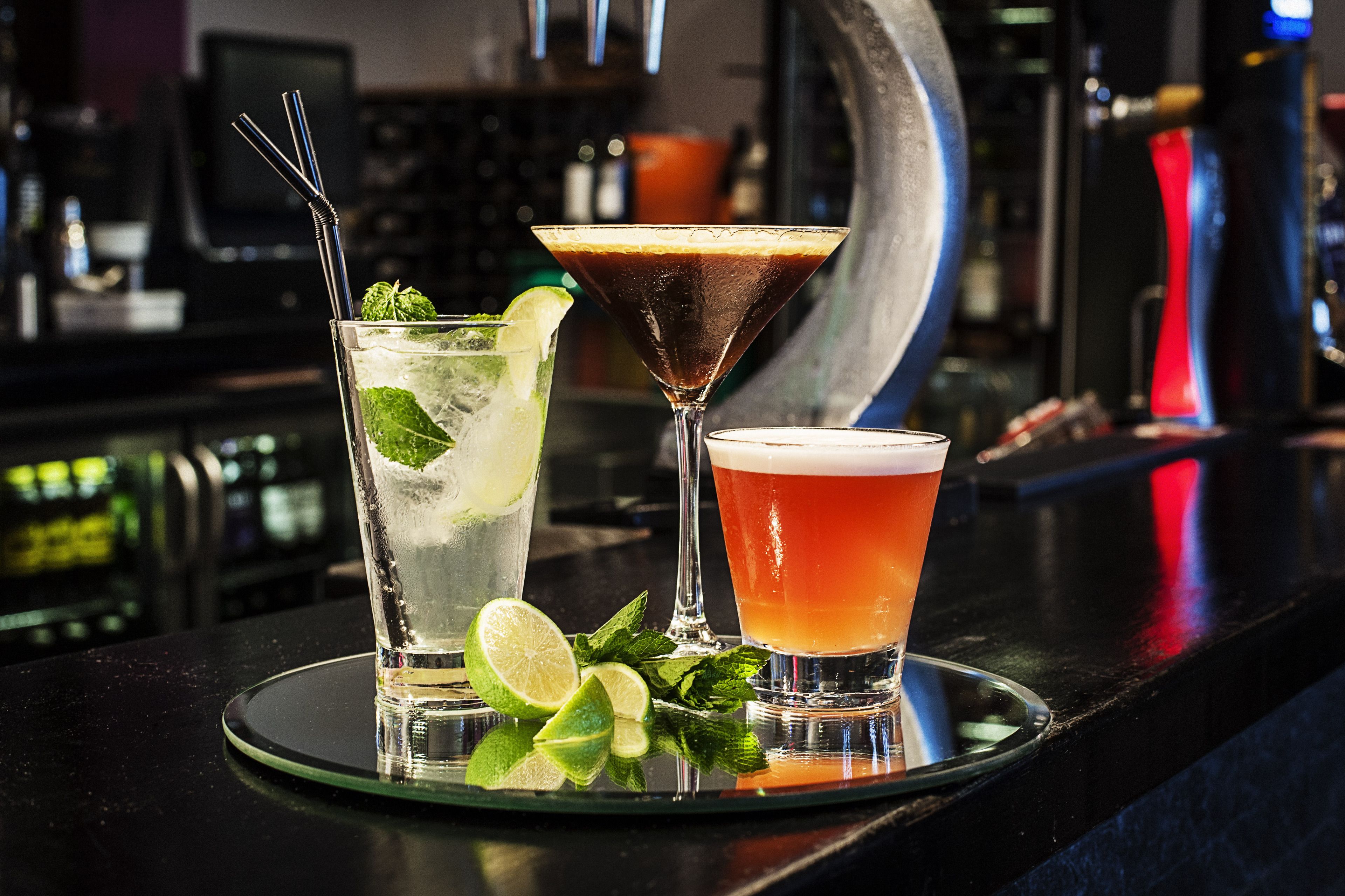 Três cocktails sobre um balc ão de bar, com fundo desfocado.
