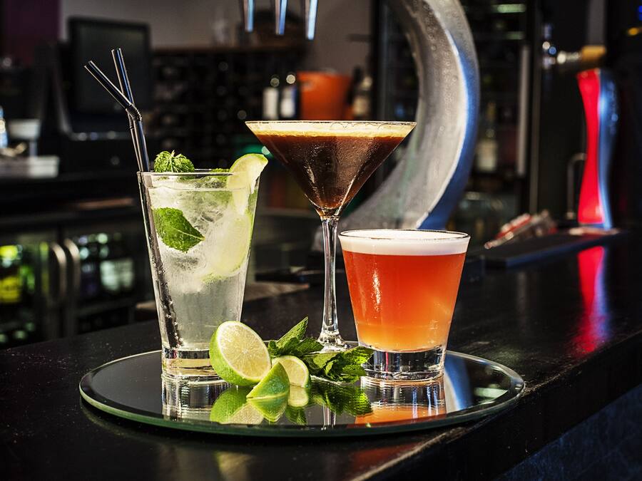 Três cocktails sobre um balcão de bar, com fundo desfocado.