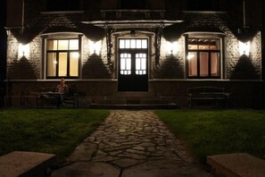 A stone building with a central entrance, two windows on either side, and a pathway leading to the entrance.