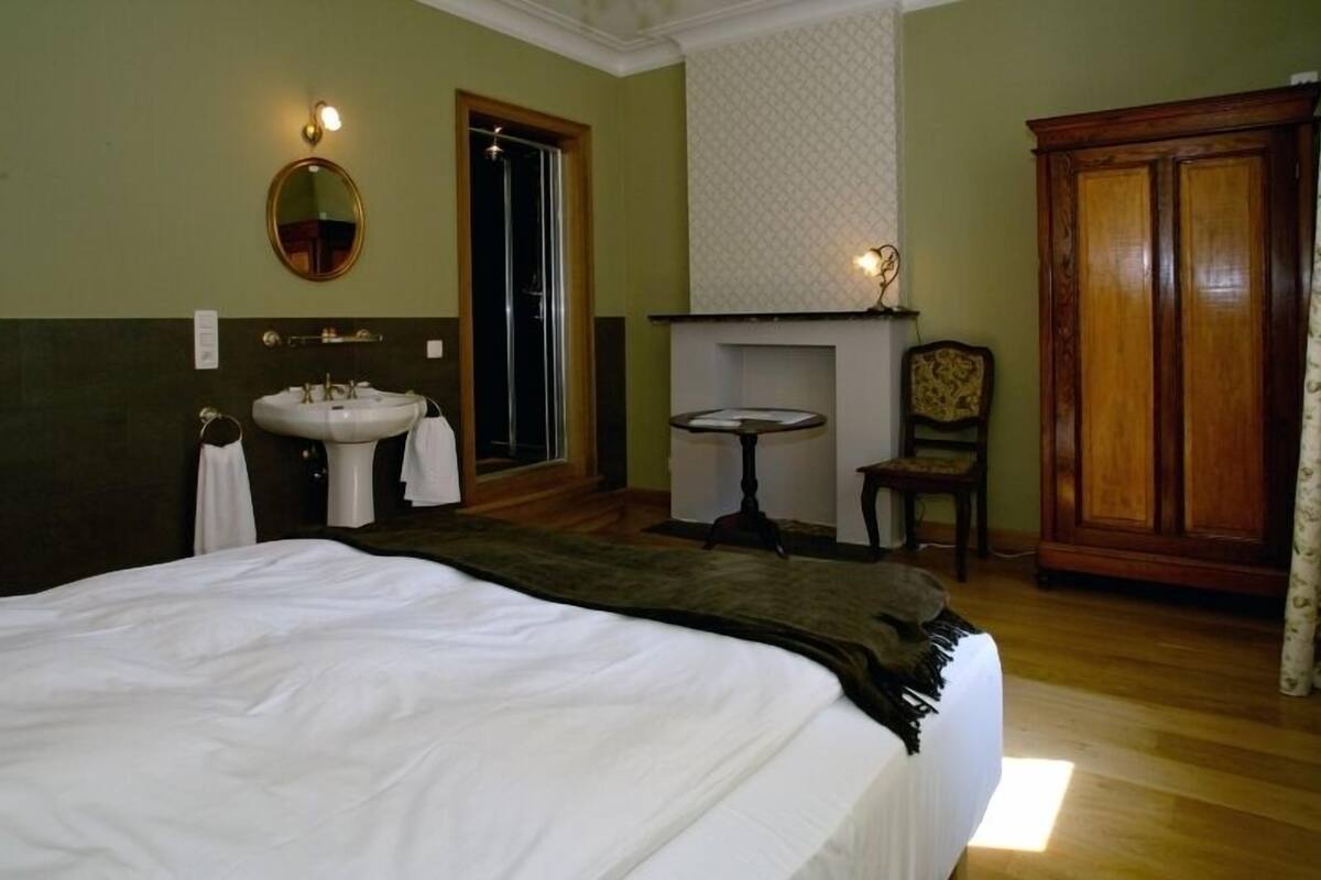 Une chambre d’hôtel avec un grand lit, un miroir rond, un lavabo, une petite table et une armoire.