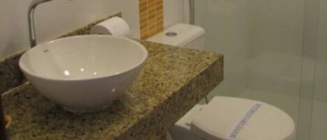 A bathroom with a granite countertop, a white sink, a toilet, and a glass shower enclosure.