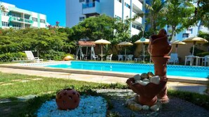 A swimming pool with lounge chairs and umbrellas, surrounded by greenery and a decorative sculpture. - Hotel La Brise (Cabo Frio)