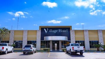 The exterior of Village Hotel with a clear blue sky and three white pickup trucks parked in front.