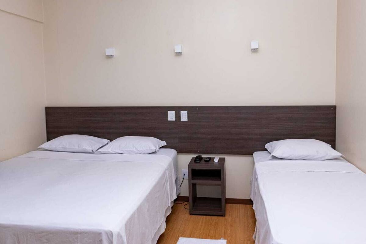Habitación doble con dos camas individuales, una mesita de noche de madera con teléfono y control remoto, y una lámpara de pared.