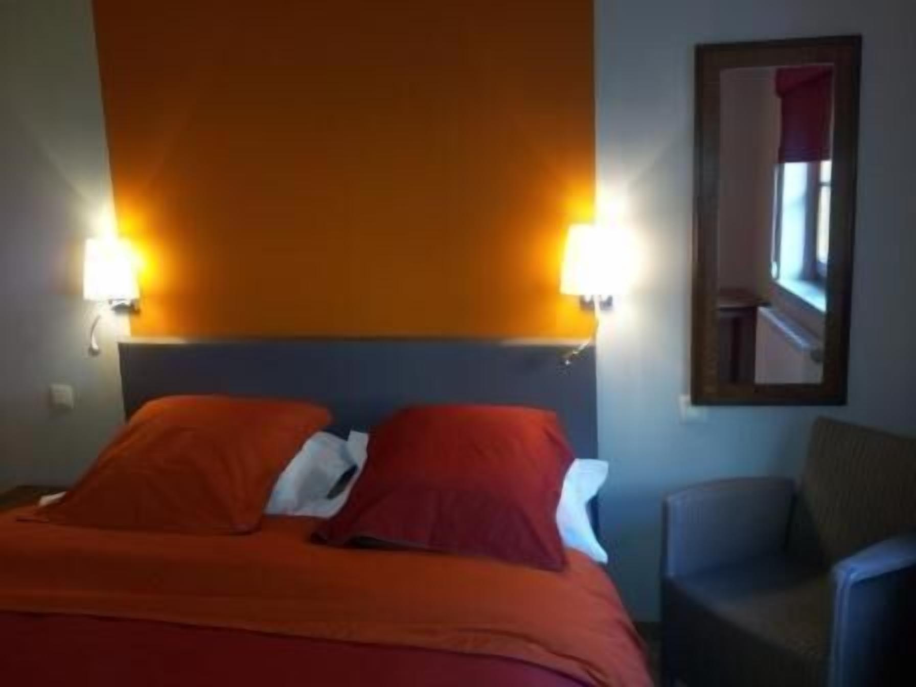 Quarto de hotel com uma cama, duas luminárias de cabeceira, uma cadeira e um espelho na parede.