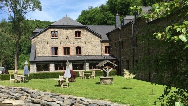 Un bâtiment en pierre doté d’un toit en pente, d’un patio couvert avec des sièges extérieurs et d’un mur en pierre sur l’un de ses côtés.
