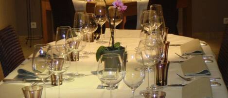 Una mesa de comedor dispuesta con varias copas de vino, platos y cubiertos, con un jarrón de flores en el centro.