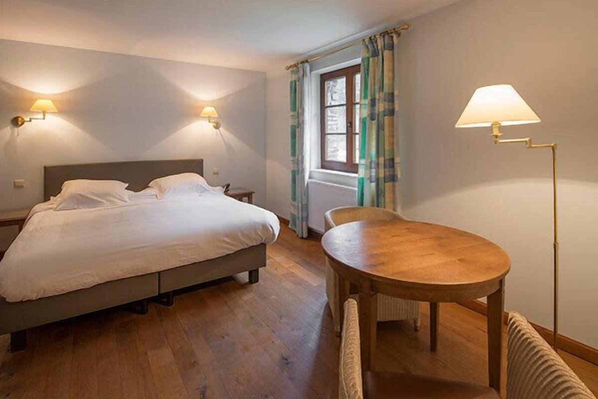 Una habitación de hotel con una cama, una mesa de madera y dos lámparas fijadas a la pared.
