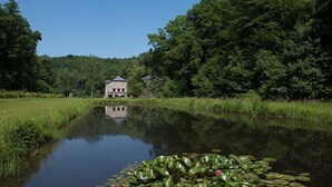 Un cadre paisible au bord d’un lac, avec un bâtiment en pierre entouré d’une végétation luxuriante et une étendue d’eau calme parsemée de nénuphars.