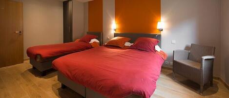 A hotel room with two beds, a chair, and a wardrobe.