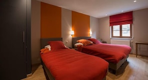 A hotel room with two beds, a window with red curtains, and a radiator.