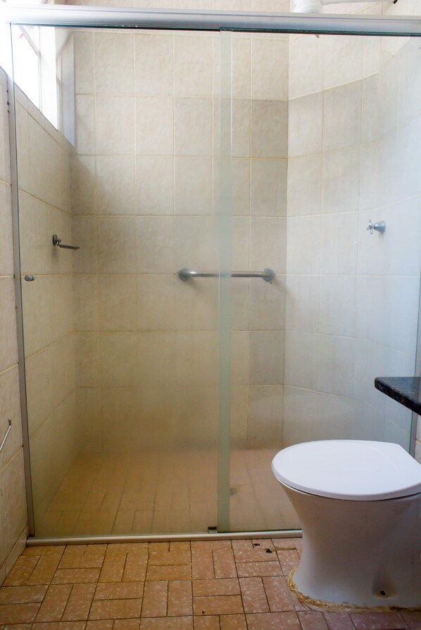 Un baño con cabina de ducha de vidrio, inodoro blanco y suelo de baldosas.