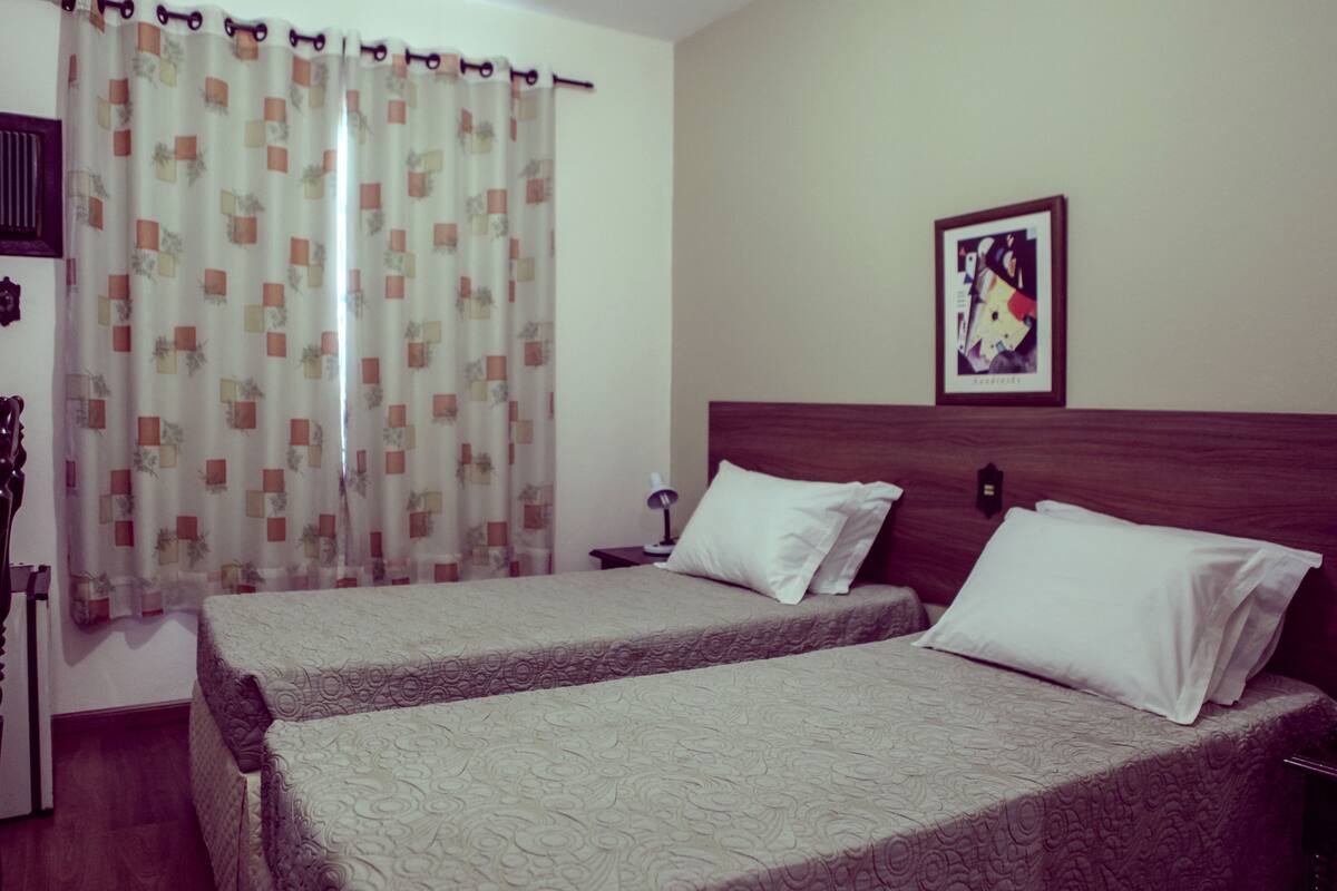 A hotel room with two beds, a wooden headboard, a nightstand, a lamp, and a framed picture on the wall.