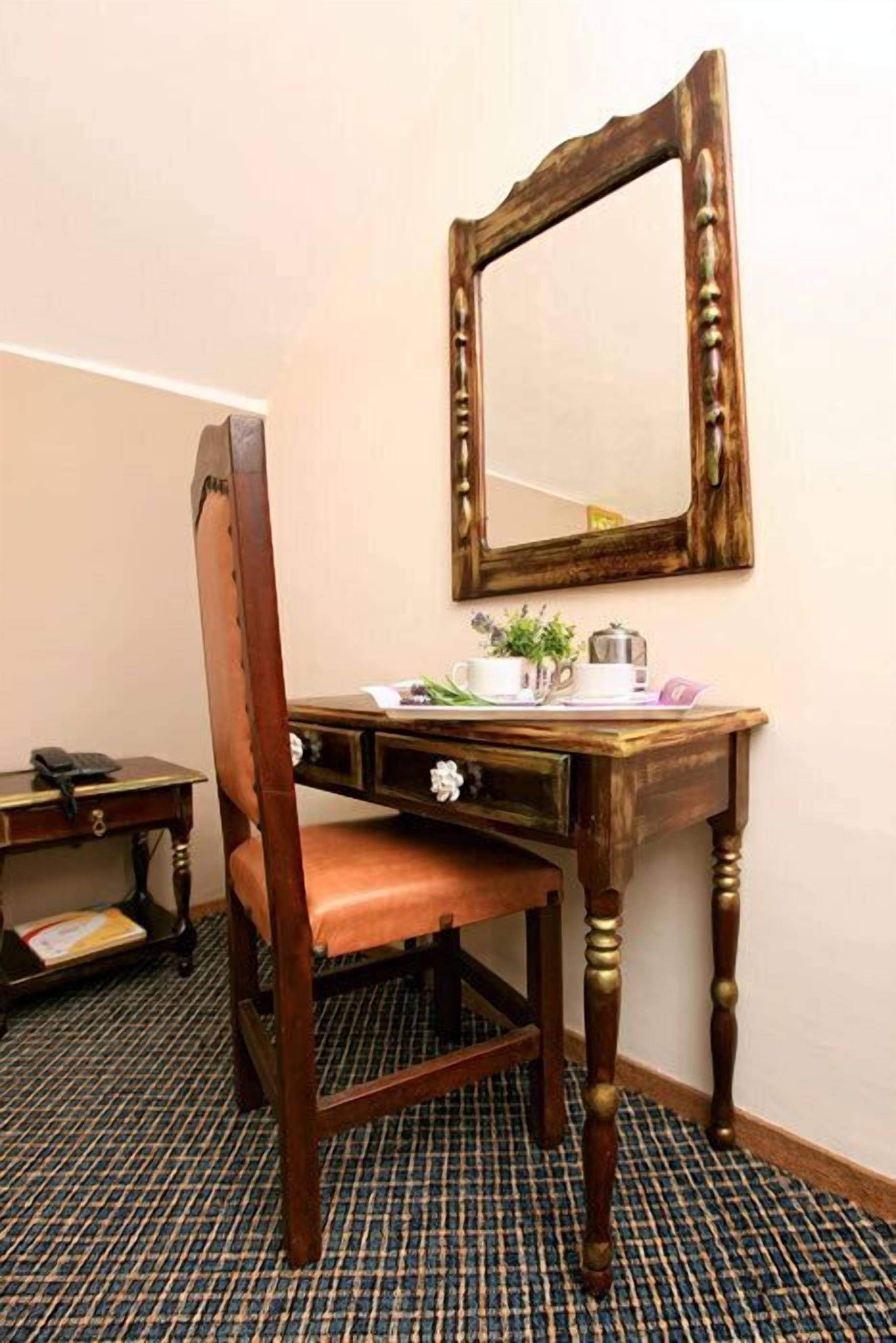 A wooden desk with a mirror, a chair, and a small table with a telephone and a book.