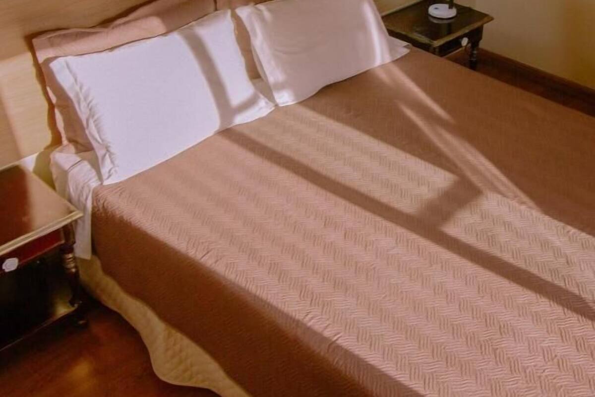 A neatly made bed with a patterned bedspread, a wooden headboard, and a nightstand with a lamp.