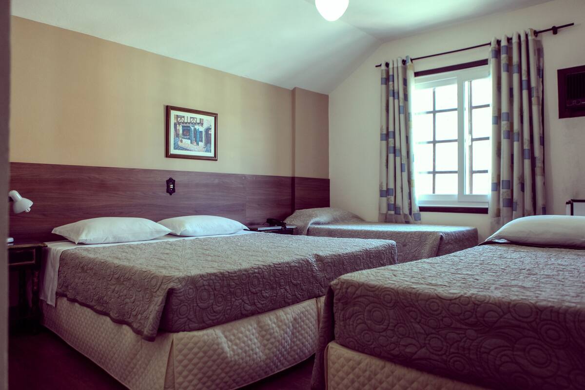 A hotel room with three beds, a framed picture on the wall, and a window with curtains.