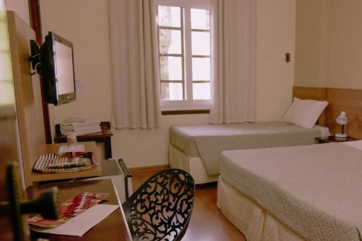 A hotel room with two beds, a desk with a chair, a window with curtains, and a framed picture on the wall.