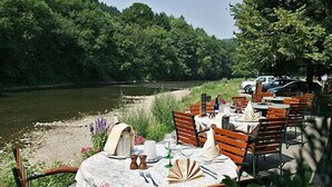 An outdoor dining area with tables set for two, overlooking a river, surrounded by lush greenery. - Hotel a la Ferme (Ferrieres)