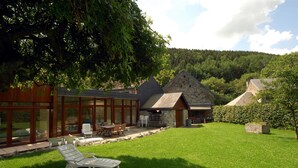 A modern house with a glass-enclosed patio, a stone building, and a lush green lawn. - Hotel a la Ferme (Ferrieres)