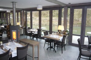 A restaurant with large windows, a fireplace, and a view of a lake. - Hotel a la Ferme (Ferrieres)