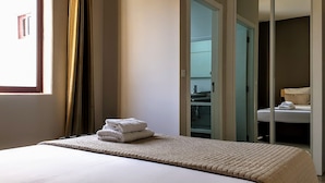Habitación de hotel con cama, ventana con cortinas, baño visible a través de una puerta abierta y una toalla sobre la cama.