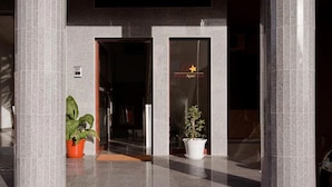 Entrada de hotel con puerta de cristal, plantas en macetas y un cartel sobre la puerta.