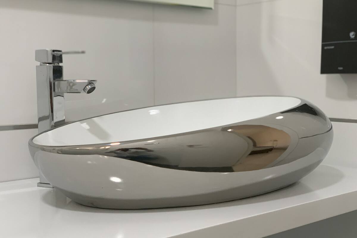 Ein modernes, ovales Waschbecken mit chromfarbenem Wasserhahn auf einer weißen Arbeitsplatte.
