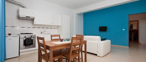 Un espace de vie compact comprenant une cuisine, un coin repas et un mur d’accent bleu.