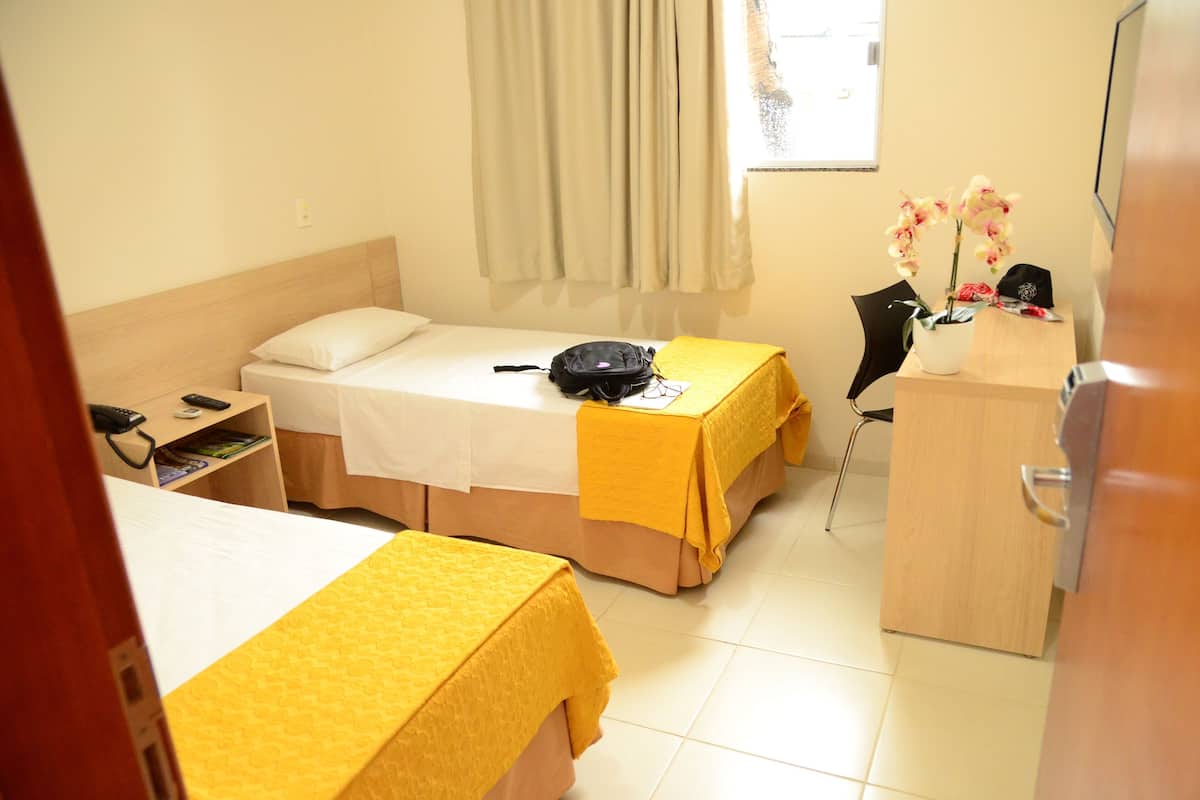 Een hotelkamer met twee bedden, een bureau, een stoel, een klein tafeltje met bloemen en een kast.