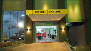 Entrada de un hotel con un cartel que dice 'HOTEL CAPITAL' y un mostrador de recepción a la vista.