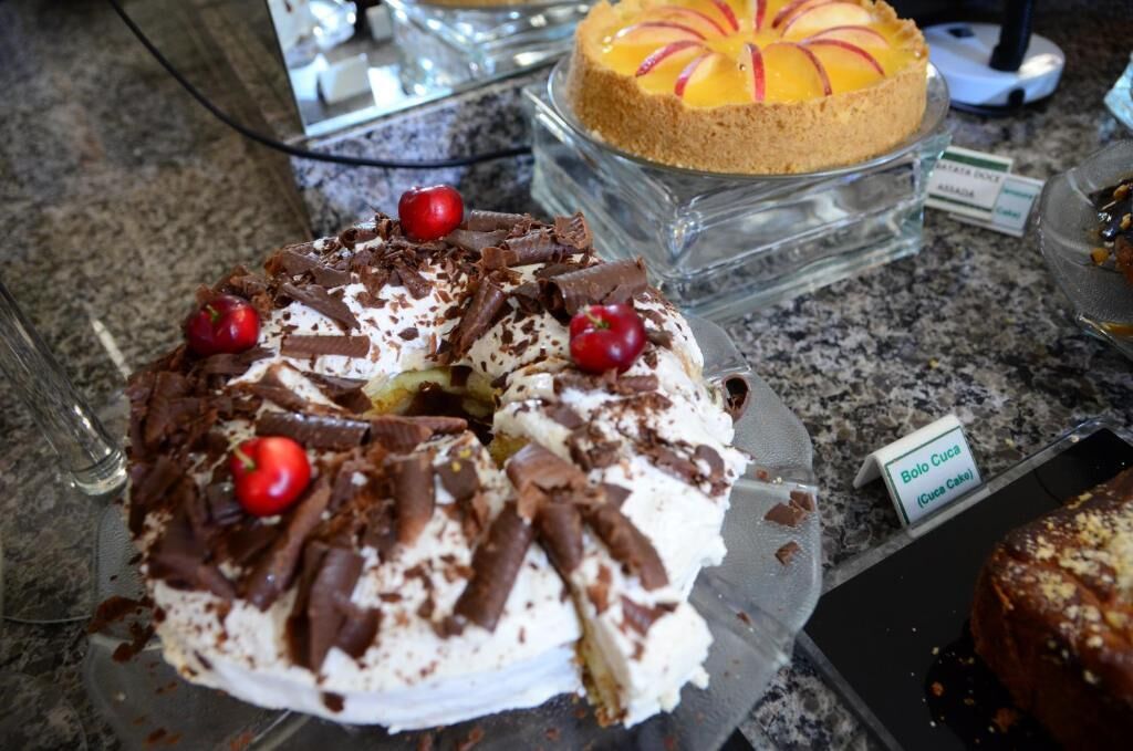 Una presentación de postres con un pastel cubierto de crema batida, virutas de chocolate y cerezas.