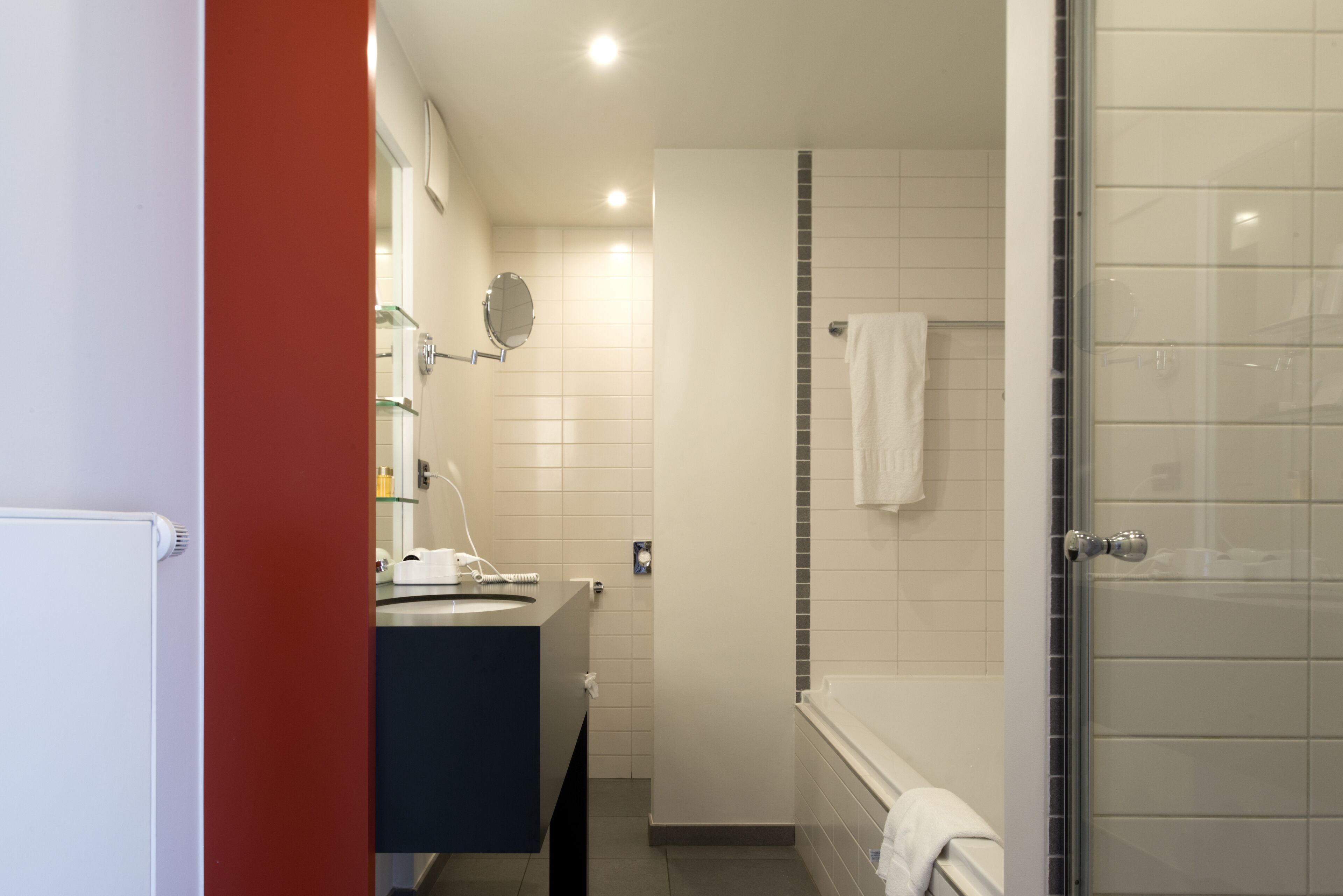 Un baño moderno con ducha, lavamanos con espejo y una toalla colgada en la pared.