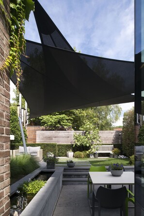 A patio area with a table and chairs, a small water feature, and a garden with a wooden fence and greenery. - Hotel Verlooy (Geel)