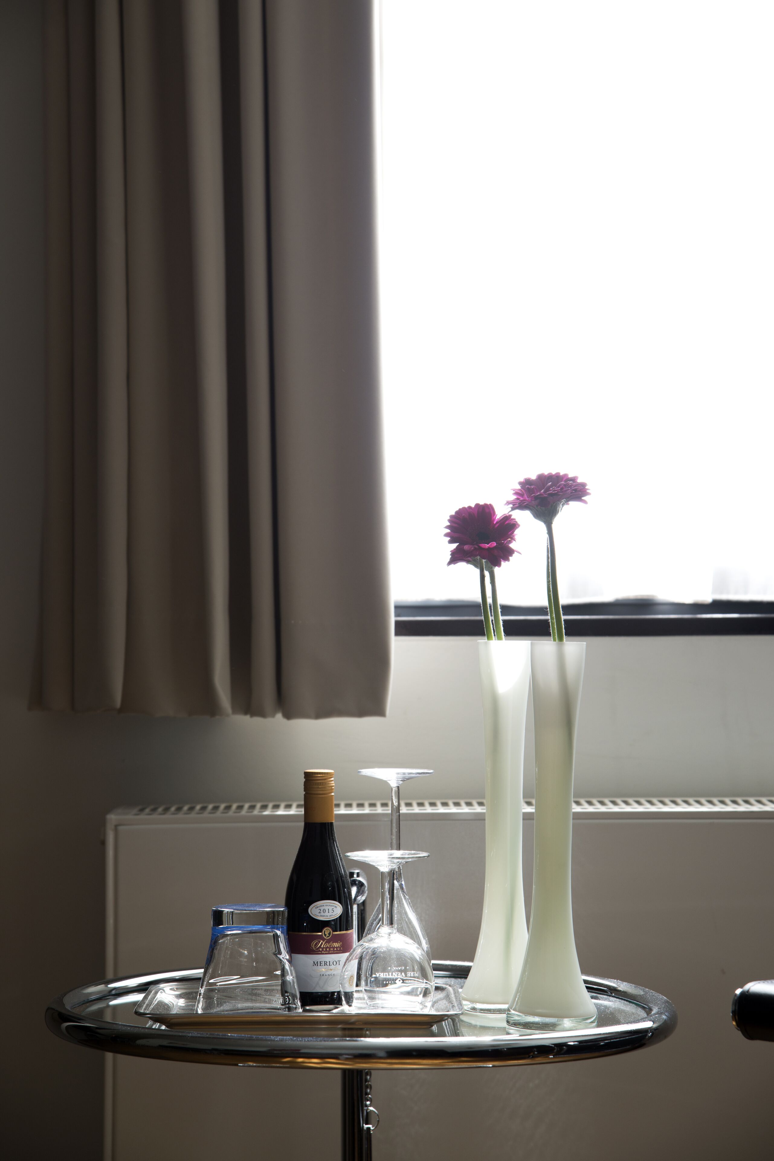 Een tafel met een fles Merlot wijn, twee vazen met bloemen en een wijnglas.