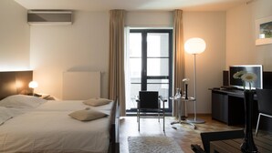 Habitació d'hotel amb dos llits, una taula de treball, una cadira, un televisor i una finestra amb cortines.