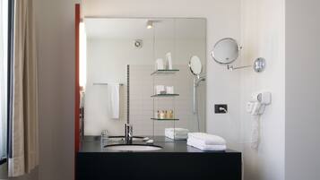 A modern bathroom with a black sink, a large mirror, a glass shelf with toiletries, a hairdryer, and a towel rack.