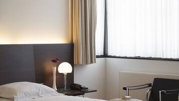Une chambre d’hôtel avec un lit, une table de chevet, une lampe et une vue sur l’extérieur à travers les rideaux.