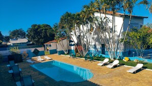 A swimming pool with lounge chairs, a stone patio, and a white building with blue trim. - Hotel Lago Azul (Bonito)