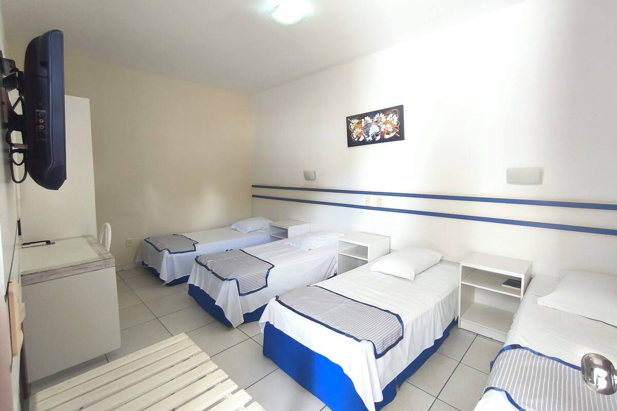 A hotel room with three single beds, a desk, a chair, a TV, and a small table.