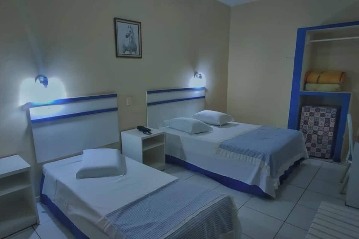 A hotel room with two beds, a nightstand, a wardrobe, and a small table.