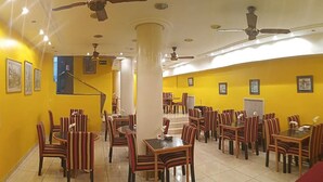 A dining area with striped chairs and tables, yellow walls, and ceiling fans. - Hotel Tres Sargentos (Buenos Aires)