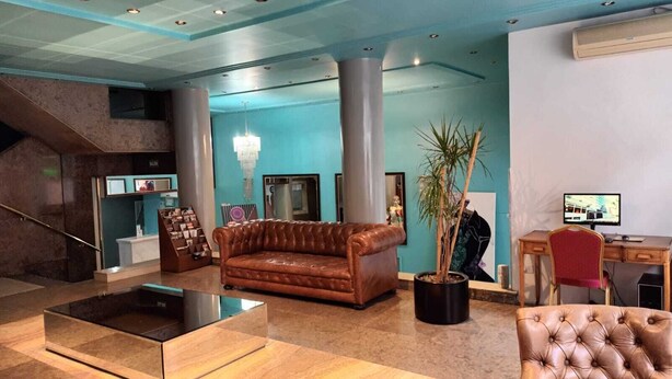 A lobby with a brown leather sofa, a glass coffee table, a potted plant, a desk with a computer, and a staircase. - Hotel Tres Sargentos (Buenos Aires)