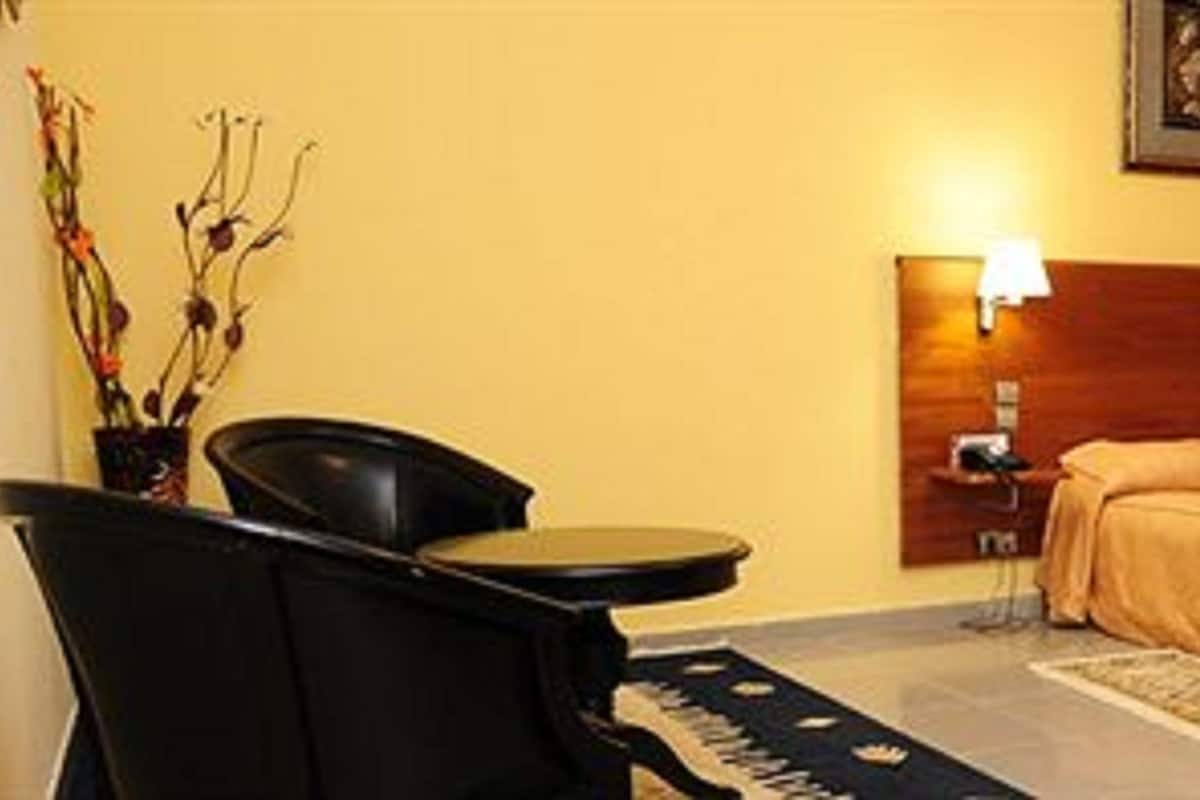 A hotel room with a bed, a chair, a nightstand, and a lamp.