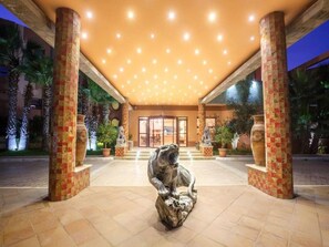 Entrada de hotel con una estatua central, palmeras y suelo de baldosas.