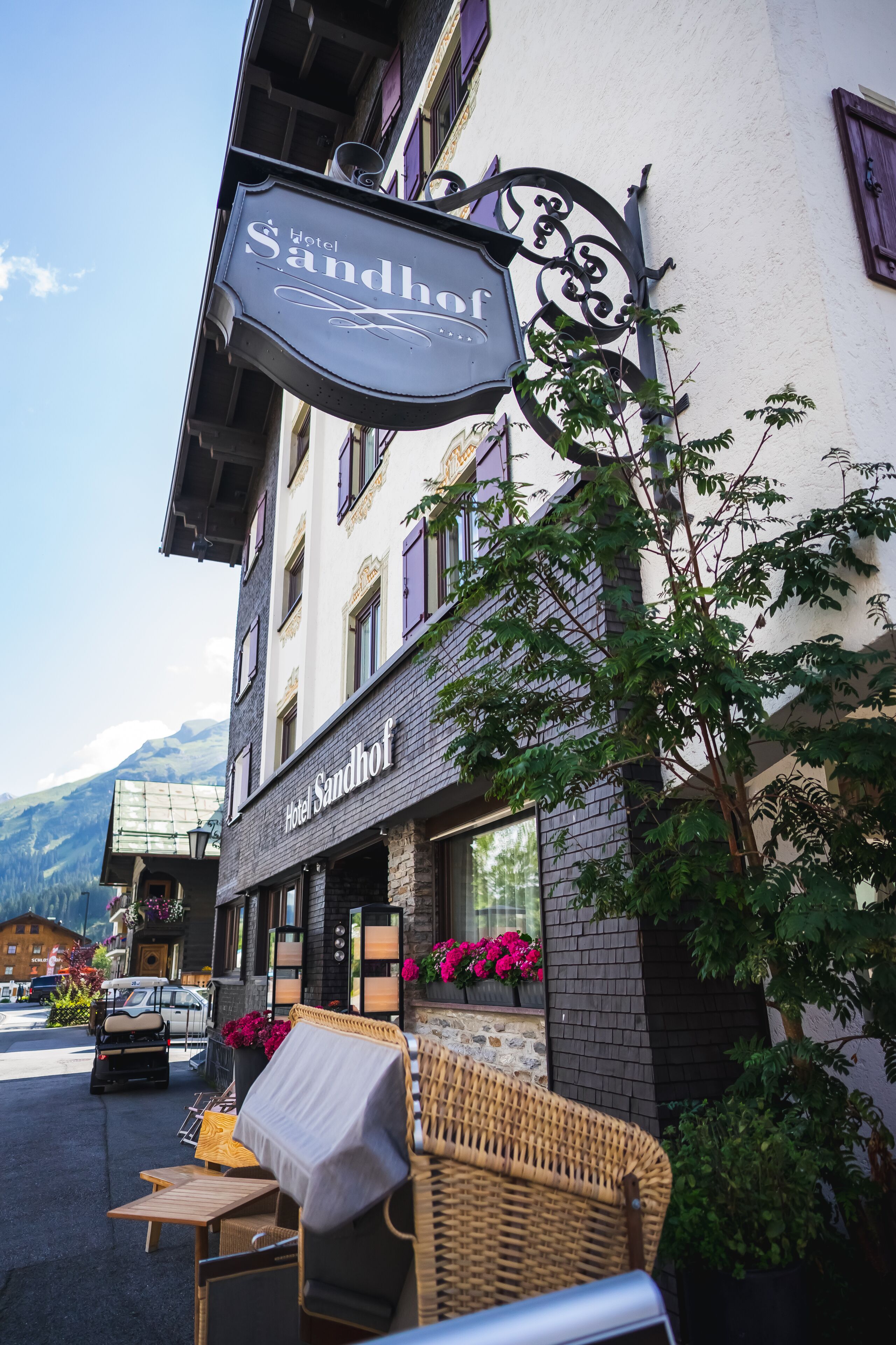 A hotel named 'Hotel Sandhof' with outdoor seating and a mountain view.